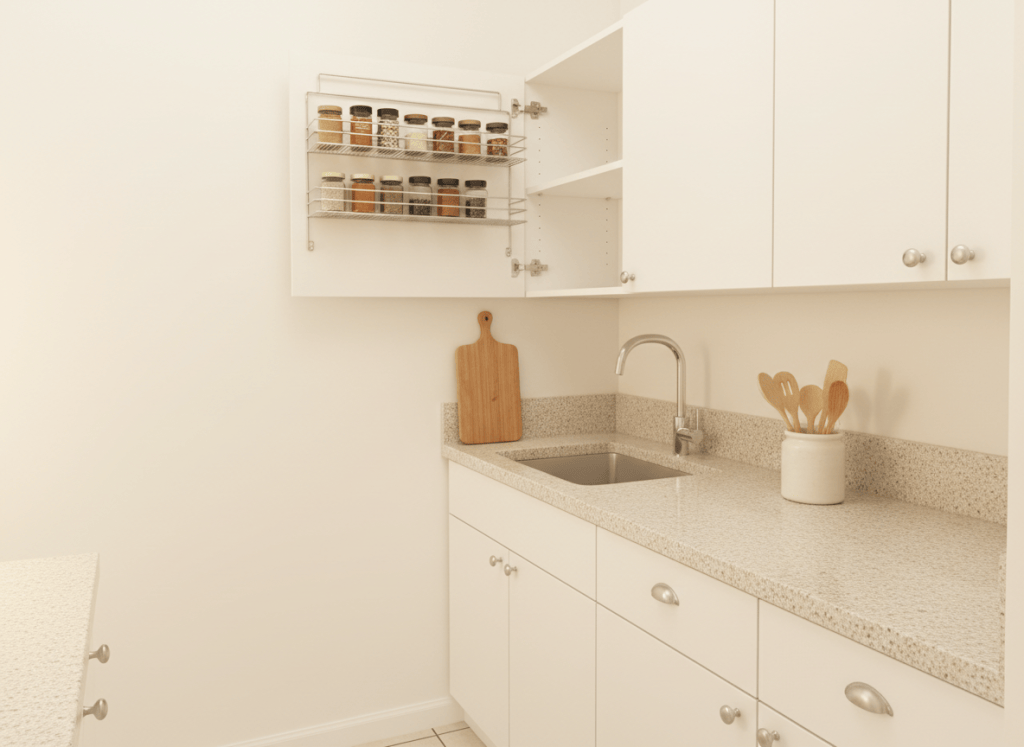 A warm, softly lit small rented kitchen corner with plain white cupboards, one cupboard door slightly open showing a wire storage rack fitted inside, clean modern style, generic unbranded design, no text, no logos, no labels, no brand names